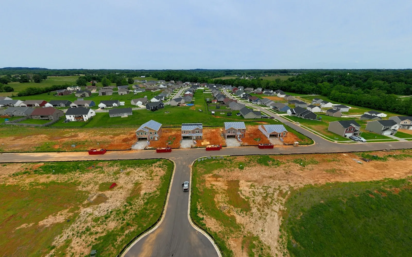 May 2025 — The first homes rise along the completed road network, documenting the transition from sitework to active building construction.